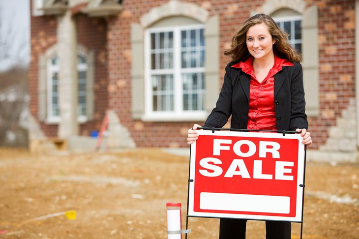 Un agent immobilier affiche un panneau à vendre devant une maison en briques en construction