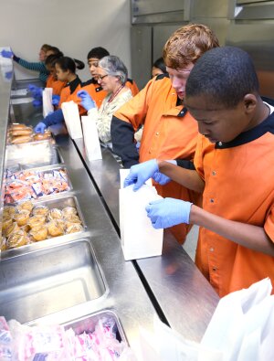 Les élèves d'un lycée de Little Rock, Arkansas aident à préparer les repas gratuits qui sont distribués aux enfants de l'hôpital pour enfants de l'Arkansas.  Les bénévoles qui préparent les repas ont des handicaps sévères et profonds, et beaucoup sont d'anciens patients.