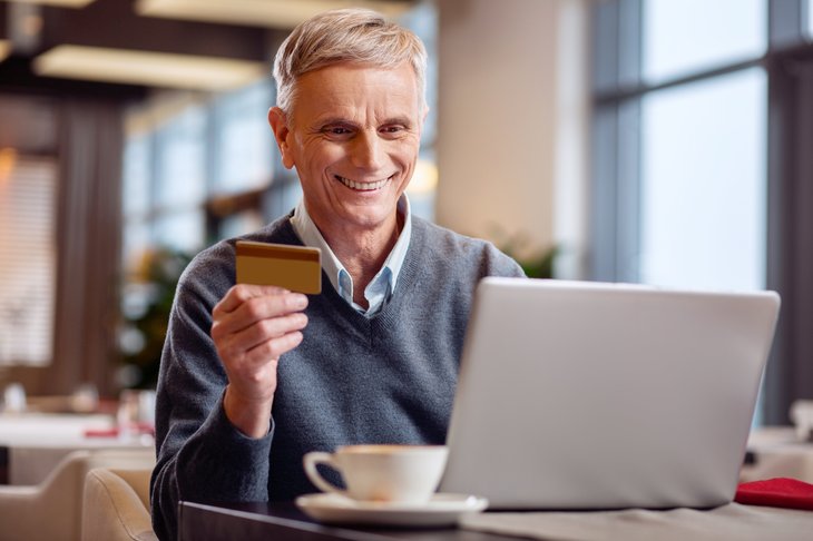 Un homme âgé tient ses cartes de crédit tout en utilisant un ordinateur portable dans un café