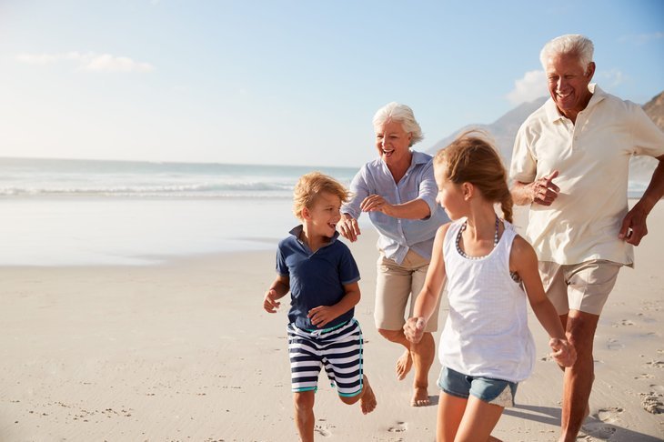 Couple de personnes âgées à la retraite courant sur la plage avec des petits-enfants