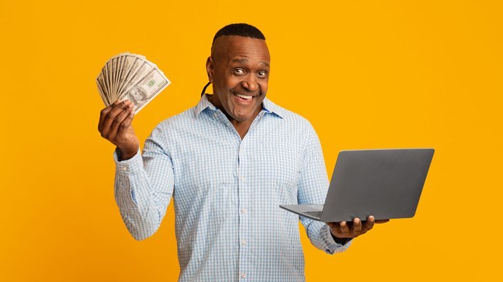 Homme excité tenant de l'argent et un ordinateur portable